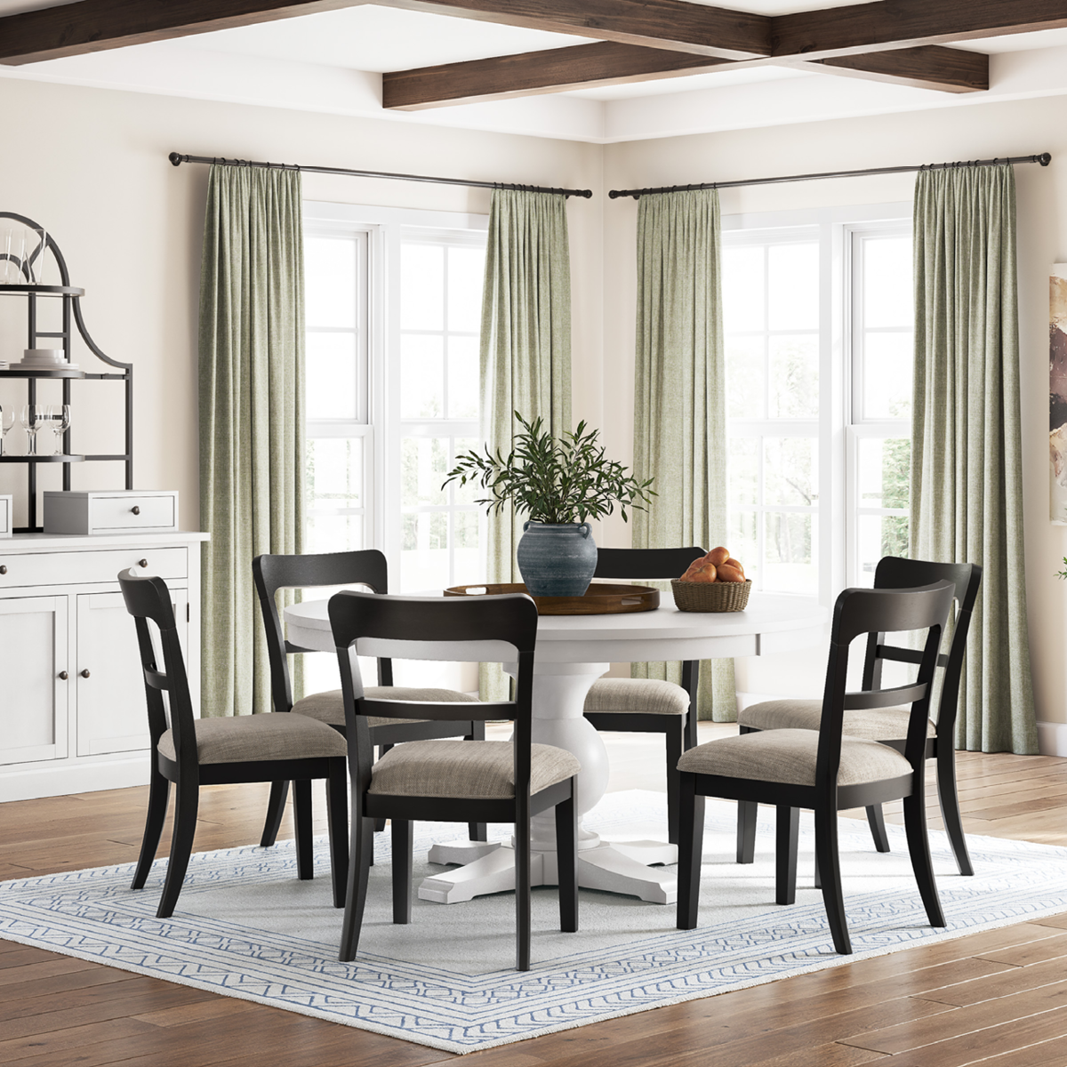 Dining room with a white table and dark wood chairs, light-colored walls, and large windows.